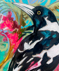 Lilli Rock Magpie Flowering Gum Coaster - A close-up painted portrait of a black-and-white bird with a long pale beak and yellow eye, set against a colourful background with pink flowers and blue-green foliage.