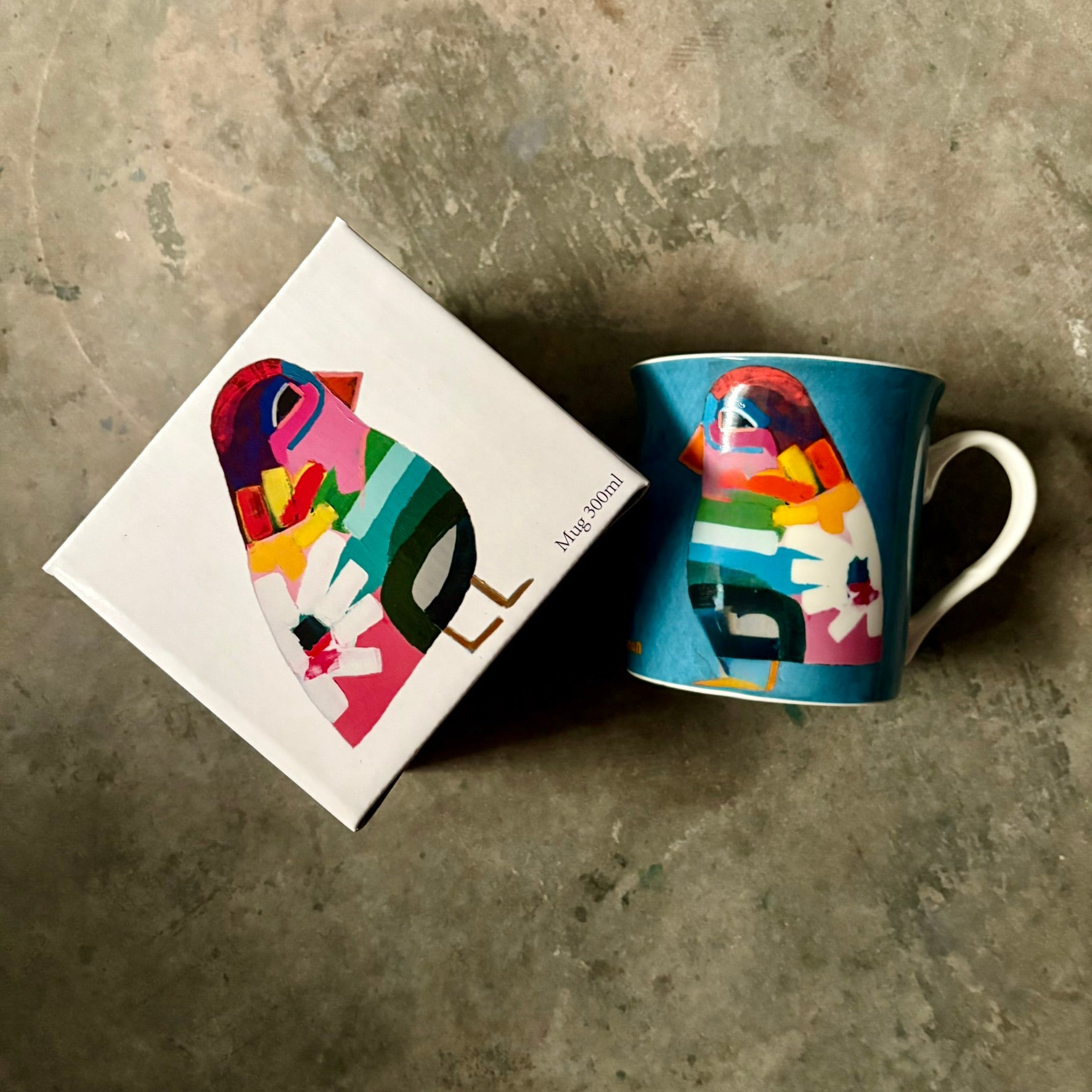Lilli Rock Mr Wilde Mug - Colourful mug with an abstract bird design next to its gift box on a textured concrete surface